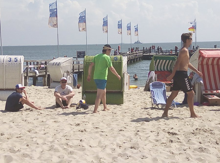 Strandkörbe und Badegäste am Nordseestrand von Wyk auf Föhr, mit Seebrücke im Hintergrund.