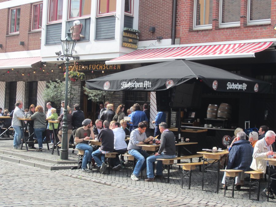 Gäste sitzen im Freien unter einem Füchschen-Schirm vor einem Düsseldorfer Brauhaus.